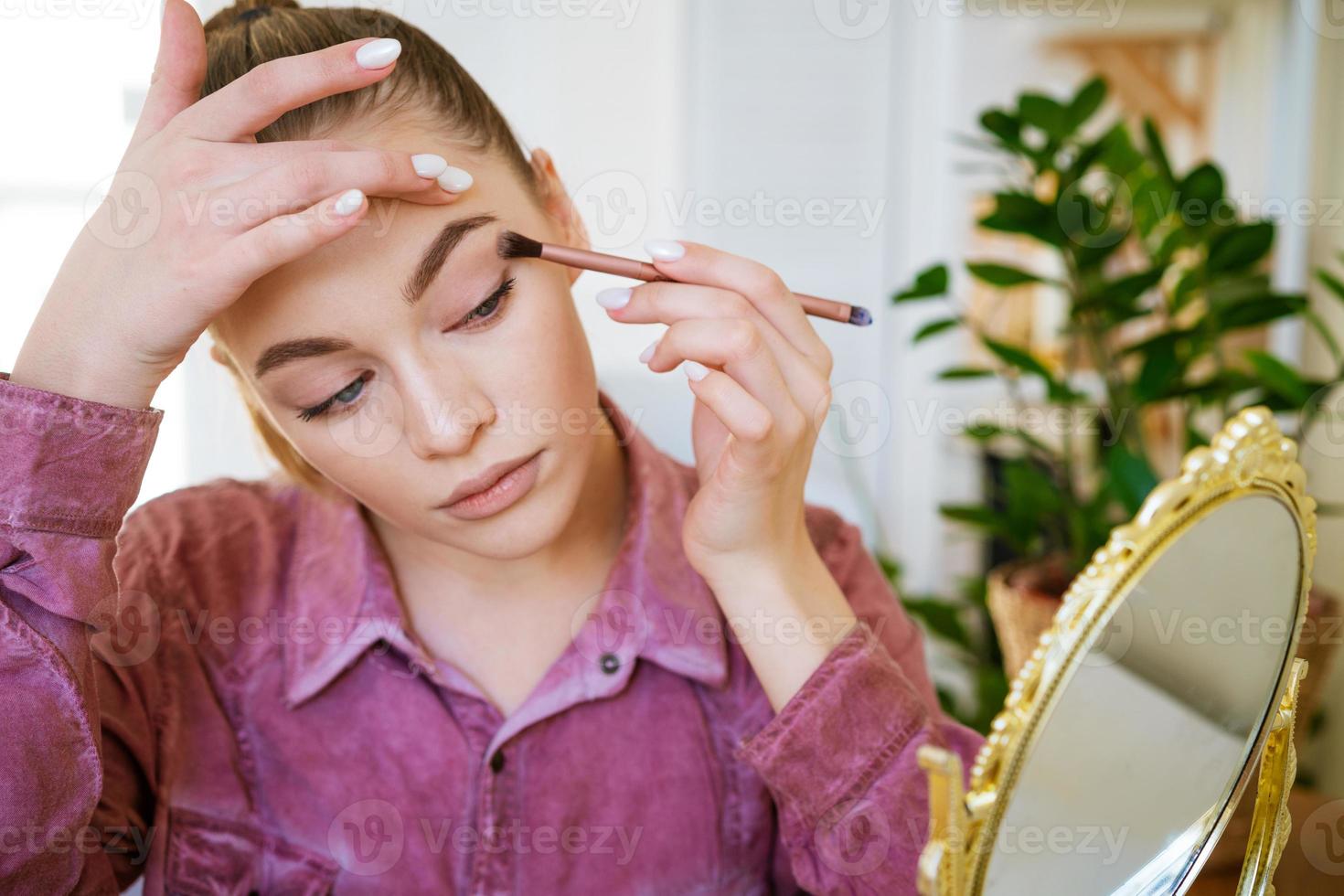 maquillaje en casa. mujer hermosa joven con pincel de maquillaje aplica sombra de ojos foto
