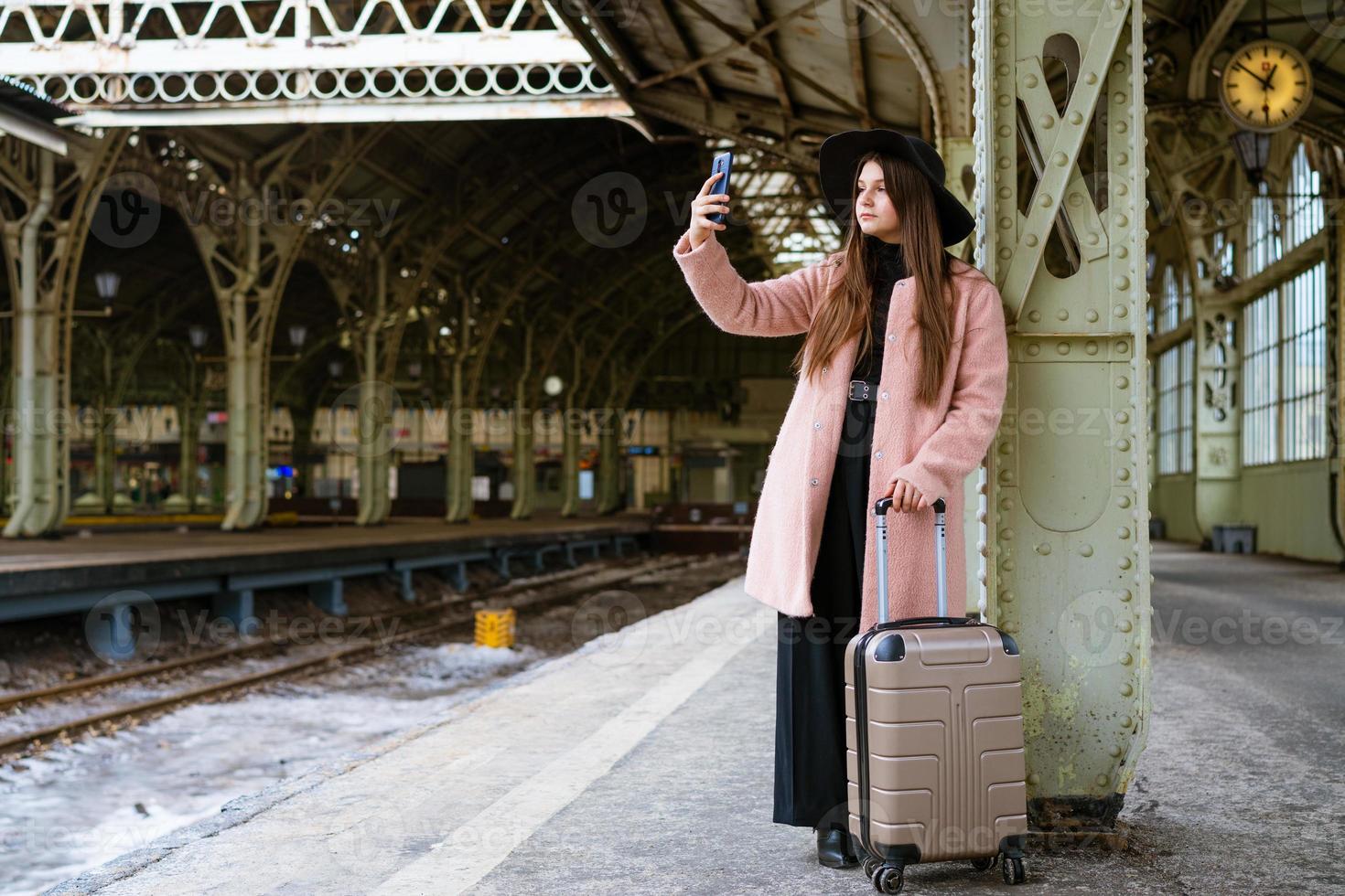 Happy young woman on platform of railway station in pink coat and black hat photo