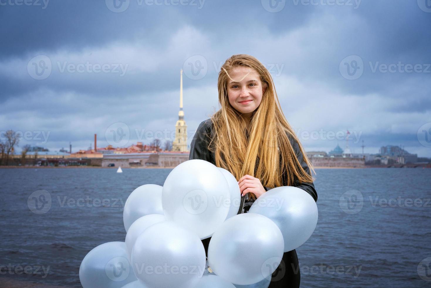 Happy cheerful girl having fun with big white latex balloons. Outdoors on the photo