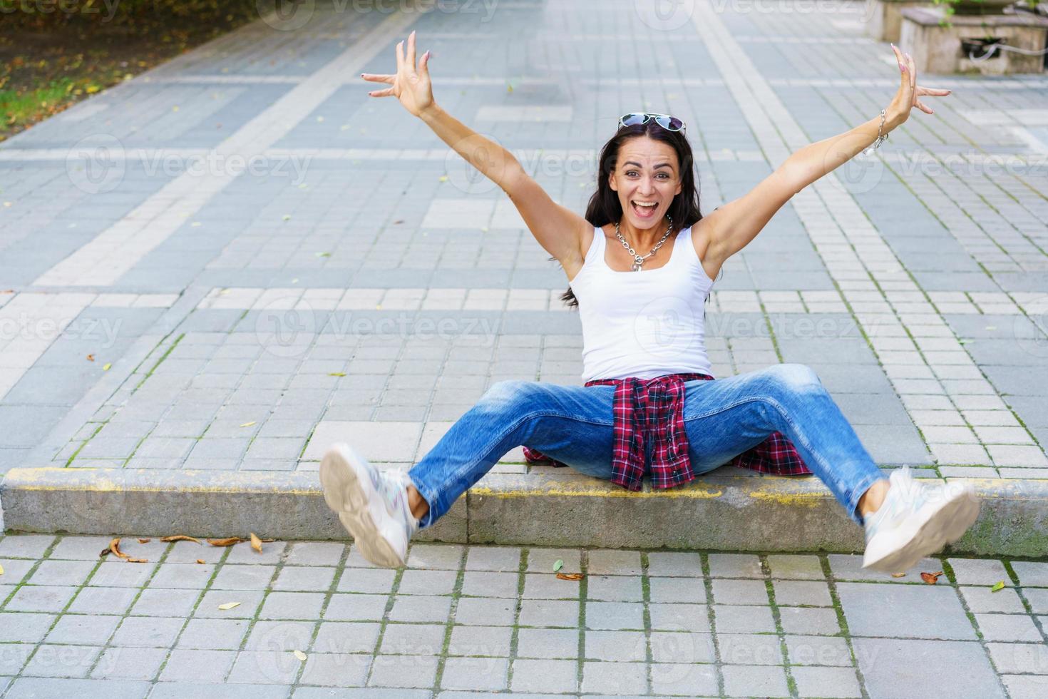 feliz moda joven mujer sentada en la acera de la calle elegante modelo femenino foto