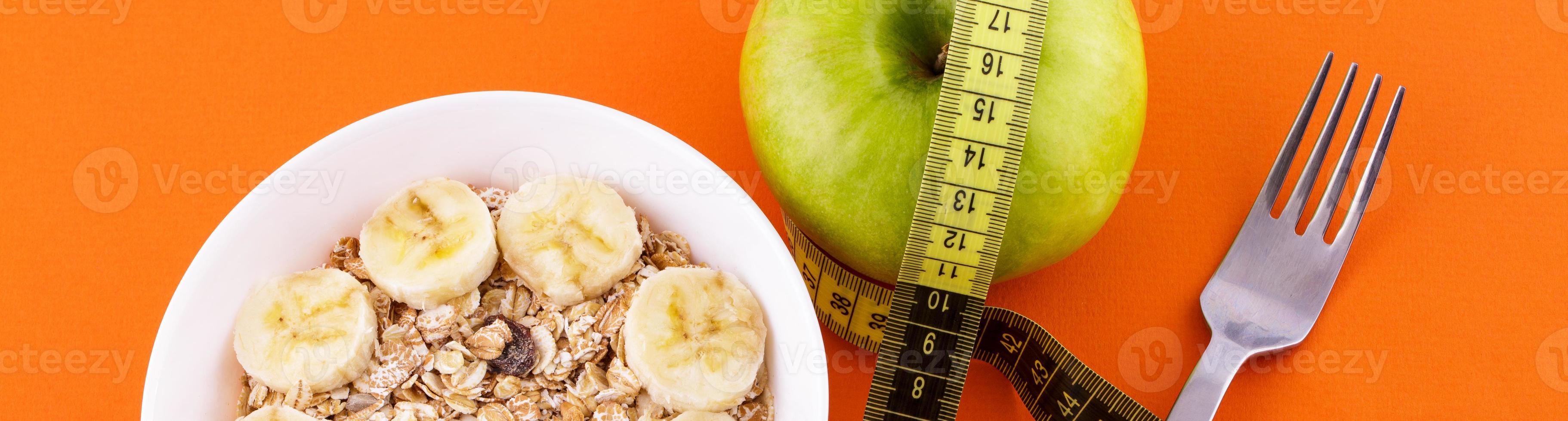 muesli with banana on orange background with apple and measuring tape photo