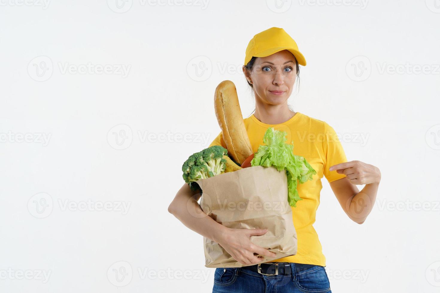 Happy delivery woman pointing at grocery bag in hand photo