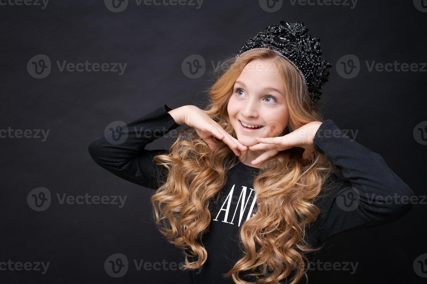retrato infantil linda chica con corona en la cabeza dobló las manos cerca de ella foto