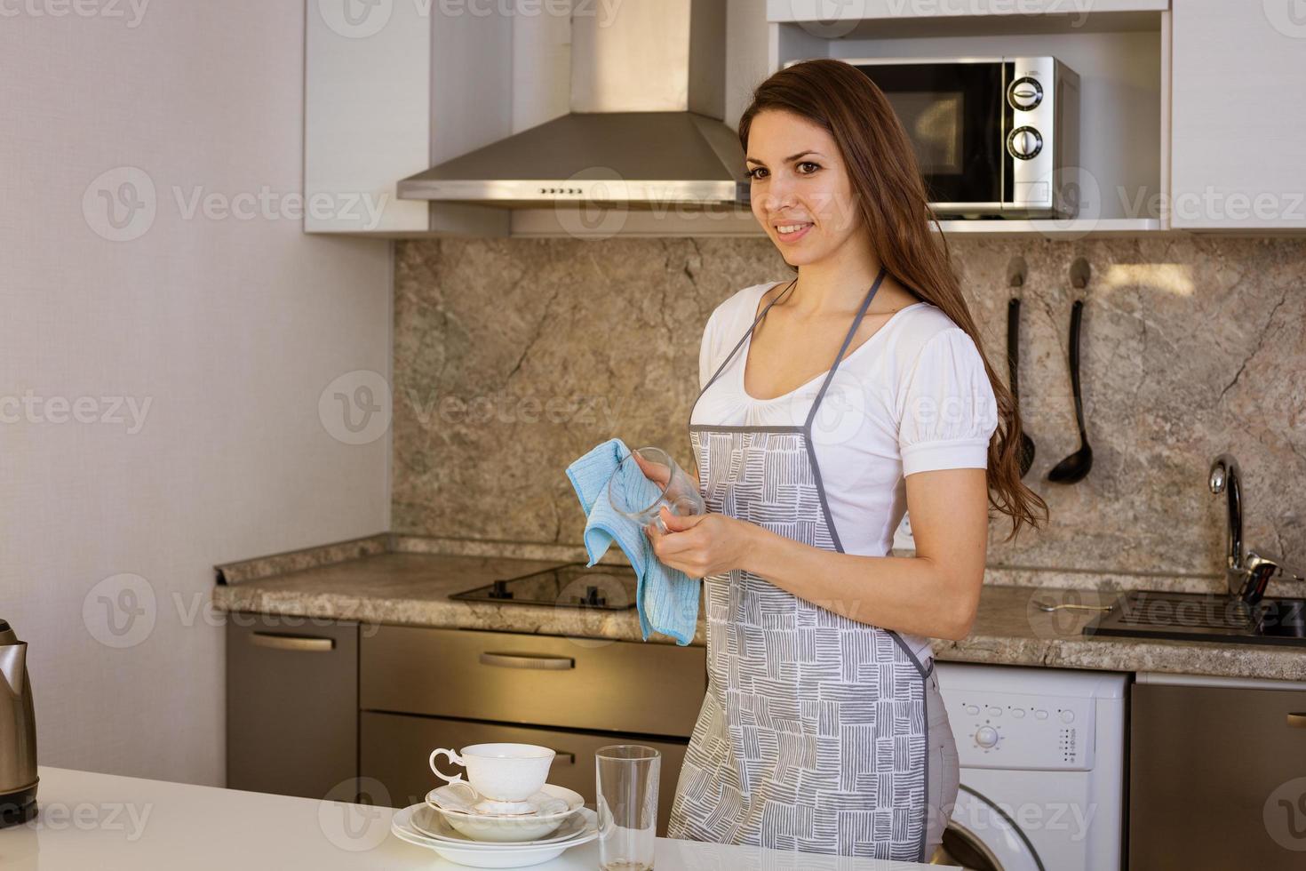 una mujer joven en una cocina moderna limpia una taza de vidrio foto