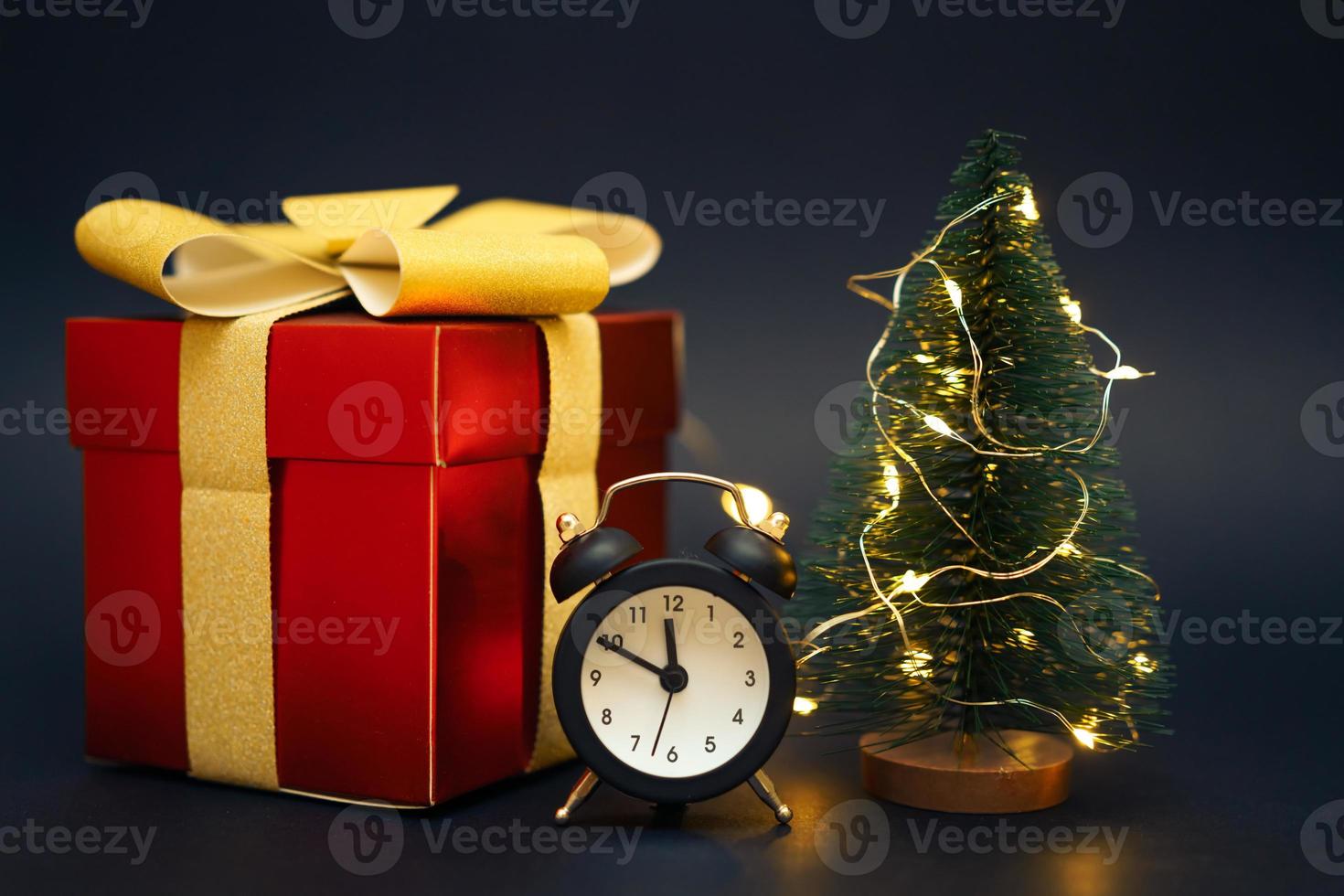 caja de regalo roja con despertador y pequeño árbol de navidad sobre fondo negro foto