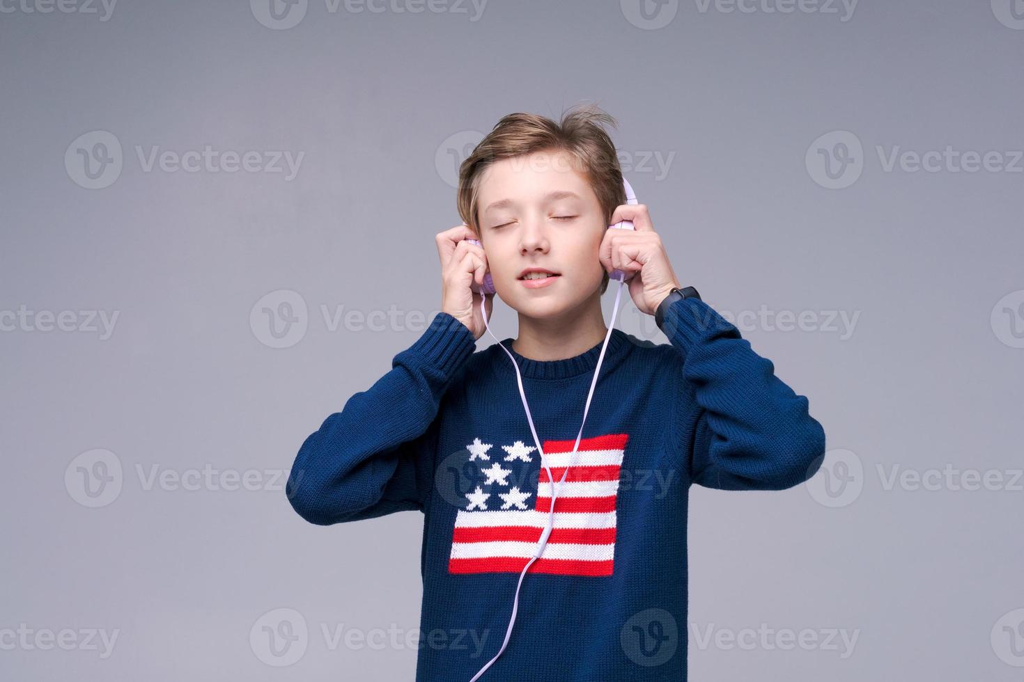Joyful guy in wired headphones listens to music in blue sweater with us flag photo