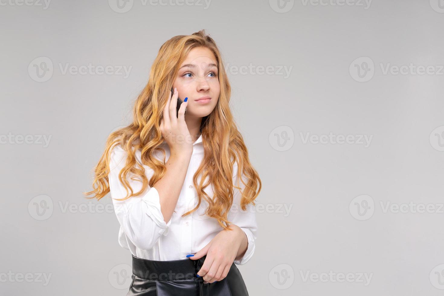 mujer joven alegre hablando por teléfono con su amiga en camisa blanca, charlando foto