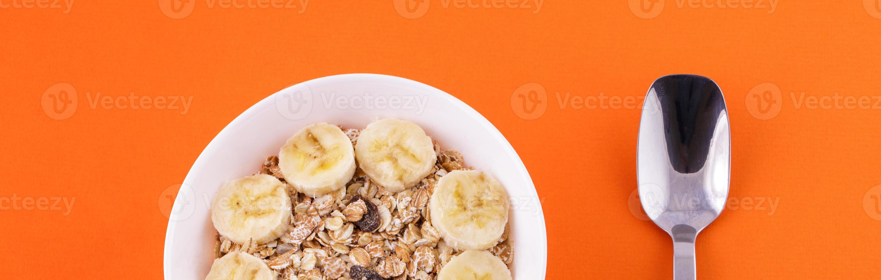 oatmeal in a plate with a banana and a spoon on an orange background photo