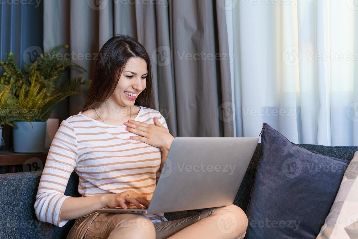 Happy girl with laptop at home on couch. Smiling young woman surfing internet photo