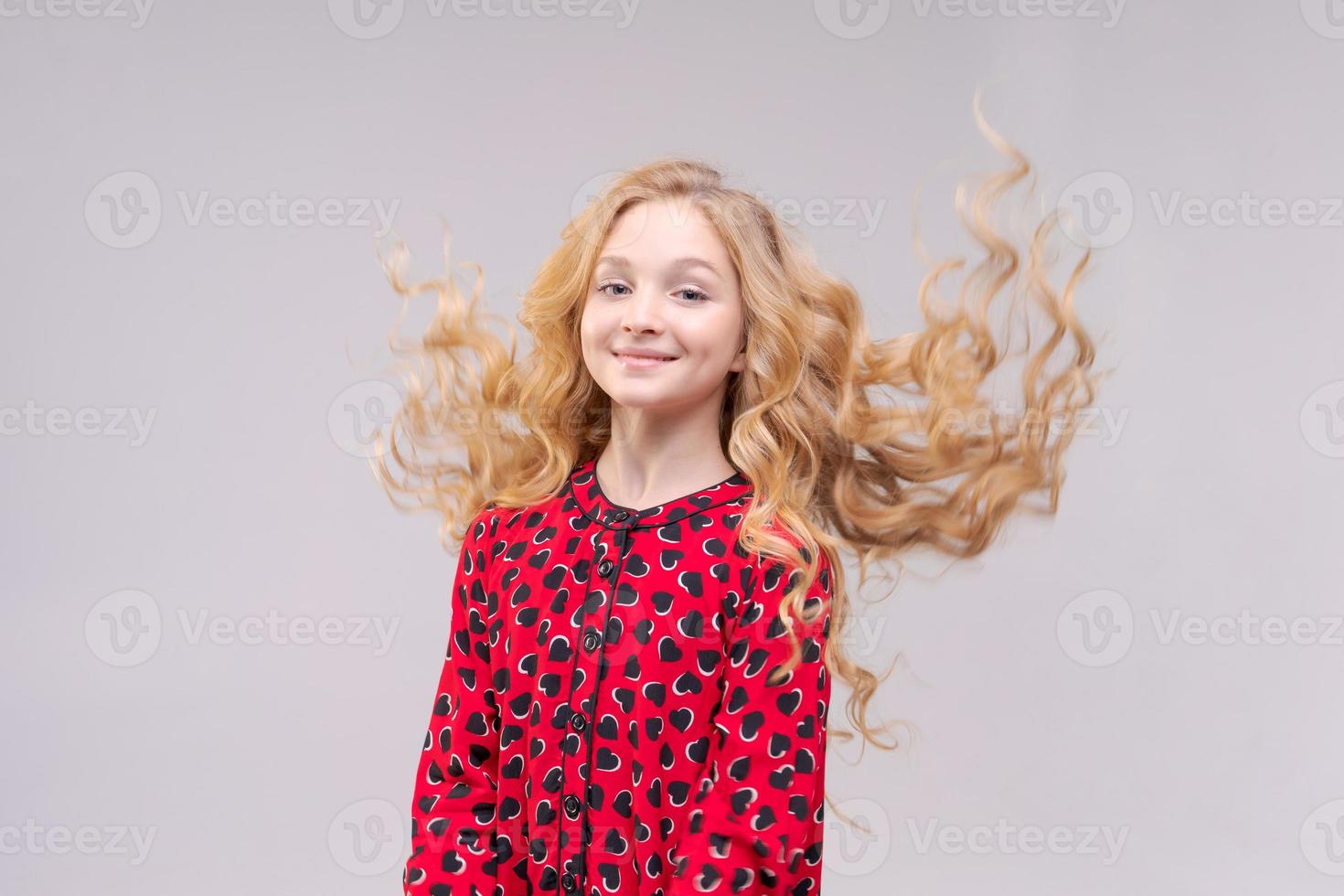 A beautiful cheerful girl in red dress with flying long wavy hair on light gray photo