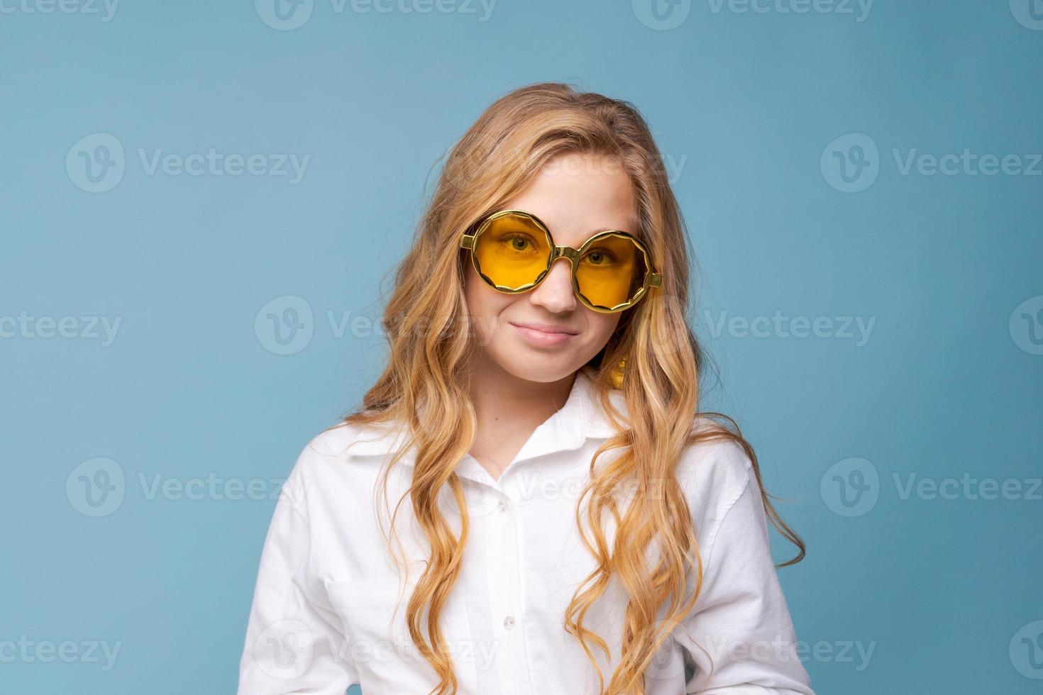 joven alegre con gafas amarillas sonriendo a la cámara contra el azul foto