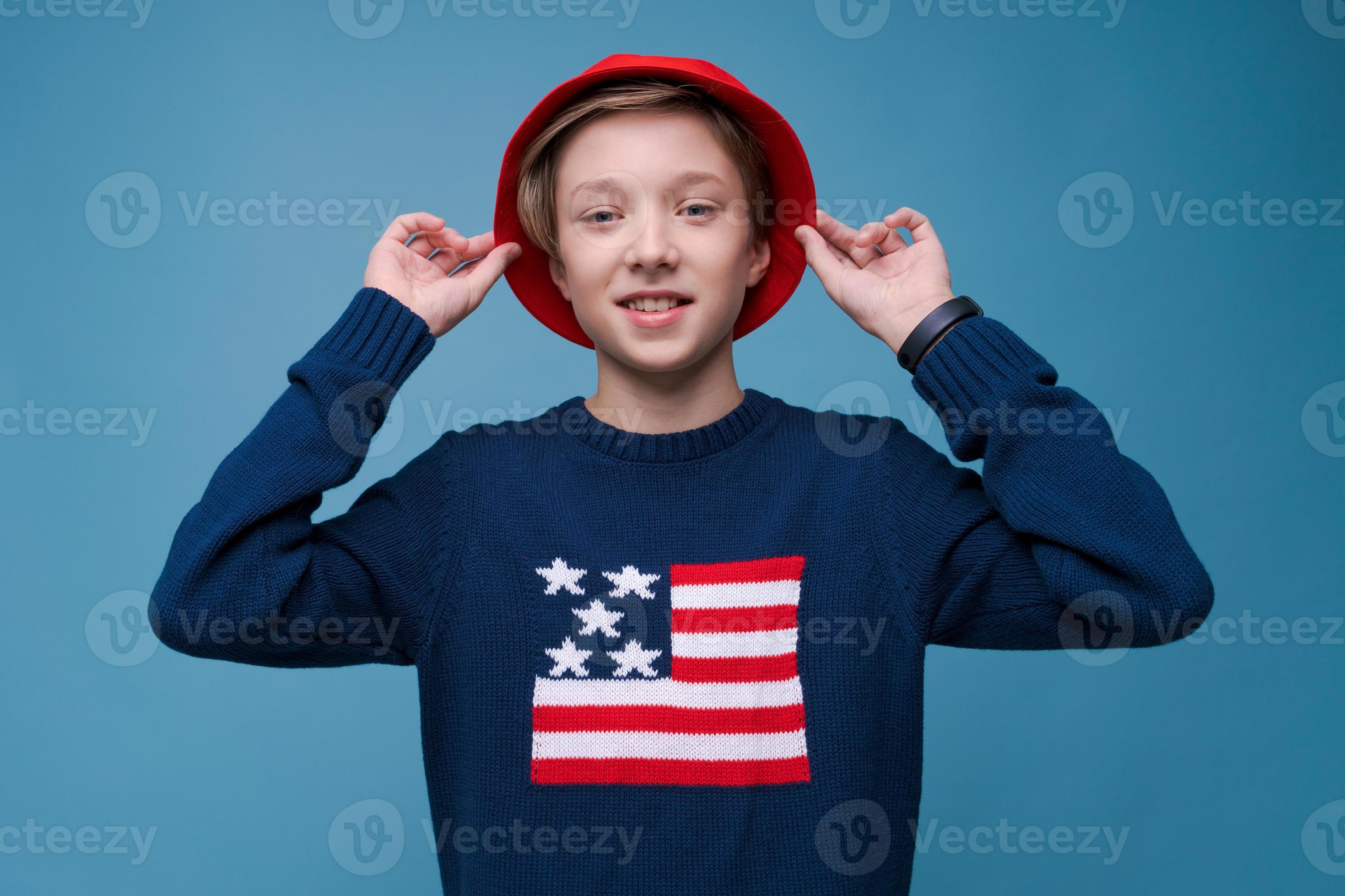 adolescente positivo en suéter azul con bandera de estados unidos y sombrero rojo sonriendo feliz foto