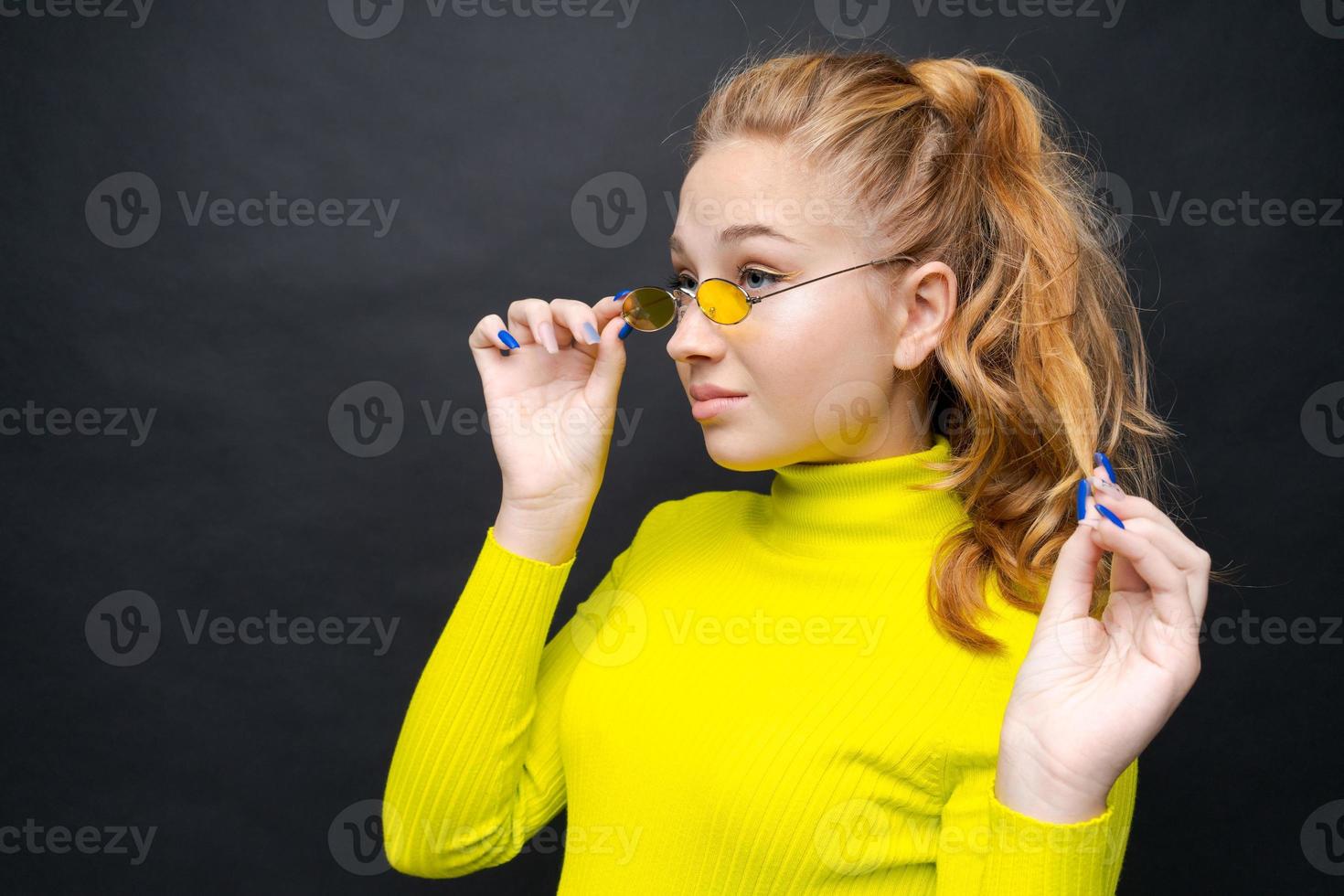 Close-up portrait happy young girl with blond hair, looks through yellow photo