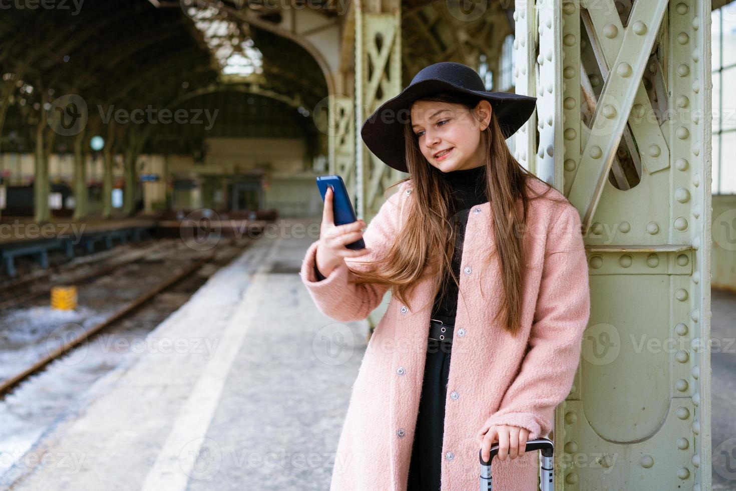 mujer joven feliz en la plataforma de la estación de tren con abrigo rosa y sombrero negro foto