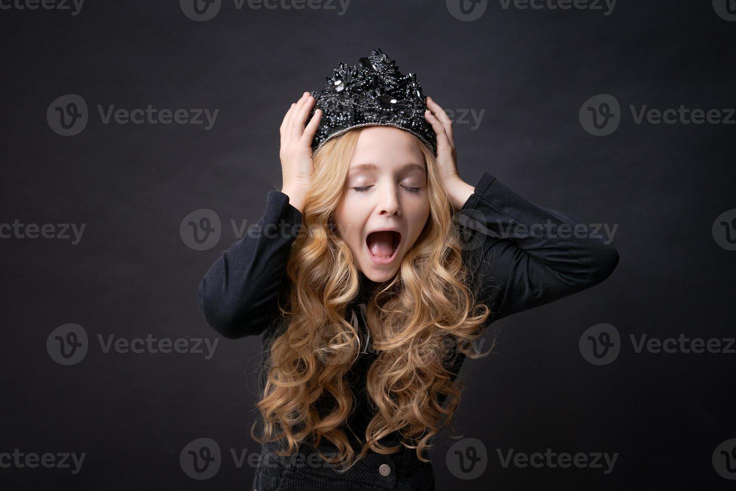 Child girl holding her hands on her head with crown with horror, closed her photo
