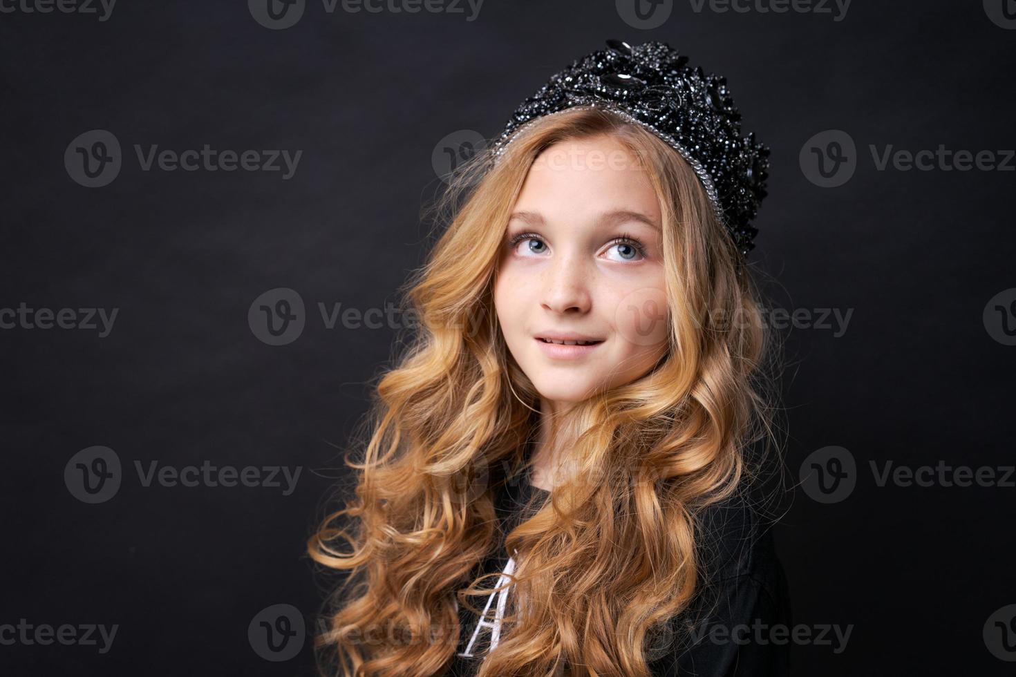Beautiful little princess girl in black clothes with a crown on her head posing photo