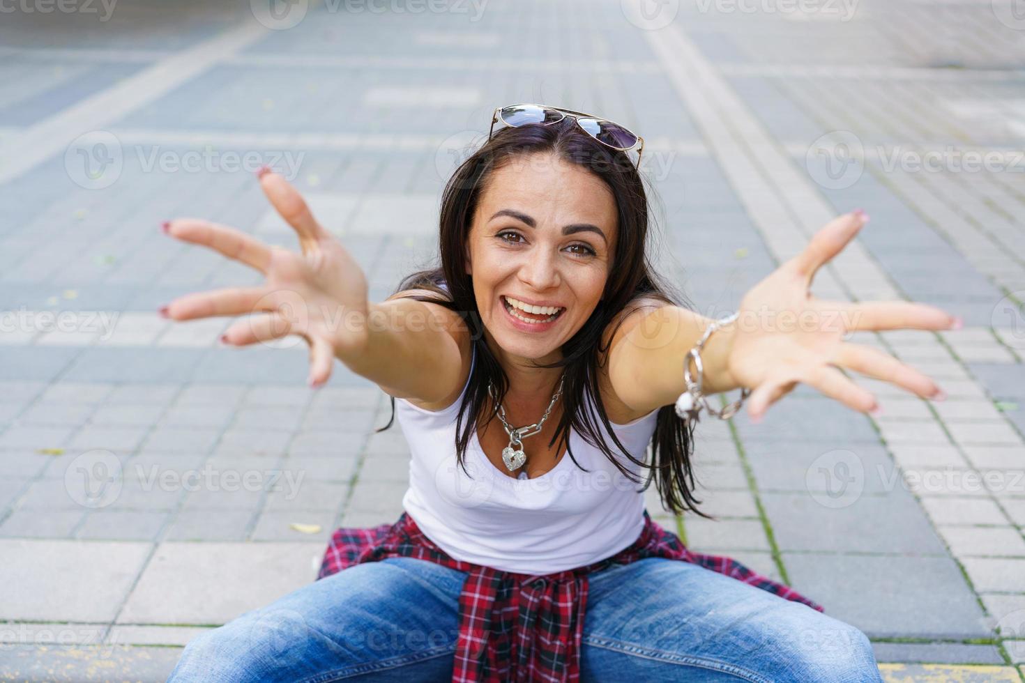 chica feliz con camiseta blanca, jeans azules y zapatillas blancas sentada en la acera foto