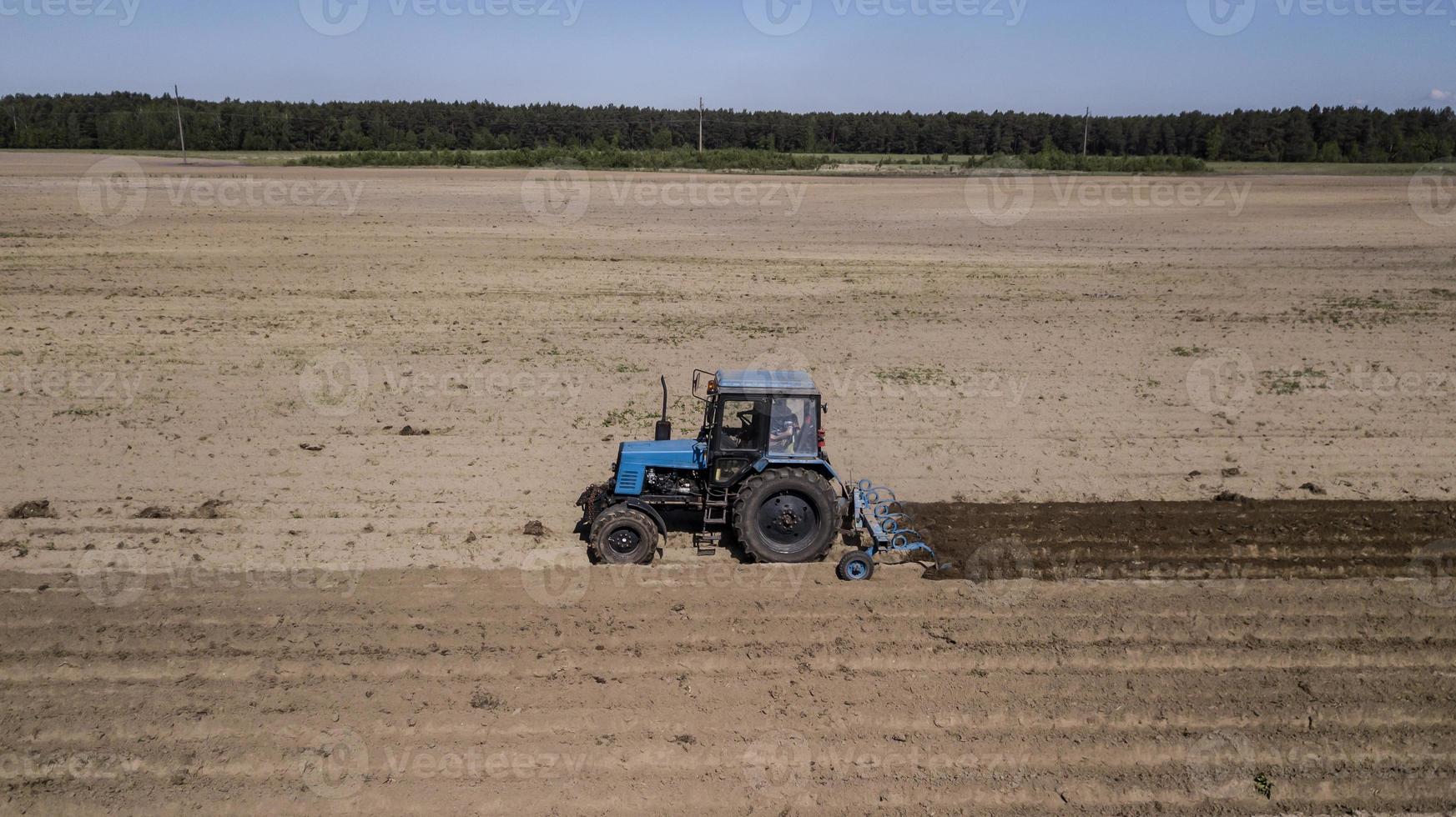 tractor - vista aérea de un tractor en el trabajo - cultivando un campo en primavera con cielo azul - maquinaria agrícola foto