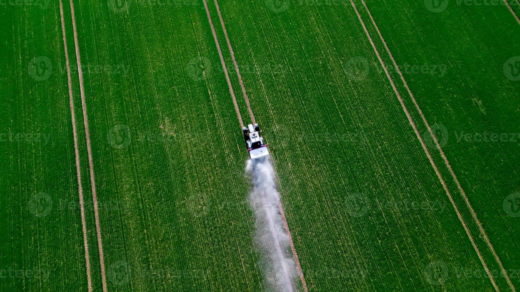 vista aérea del tractor rociando los productos químicos en el gran campo verde foto