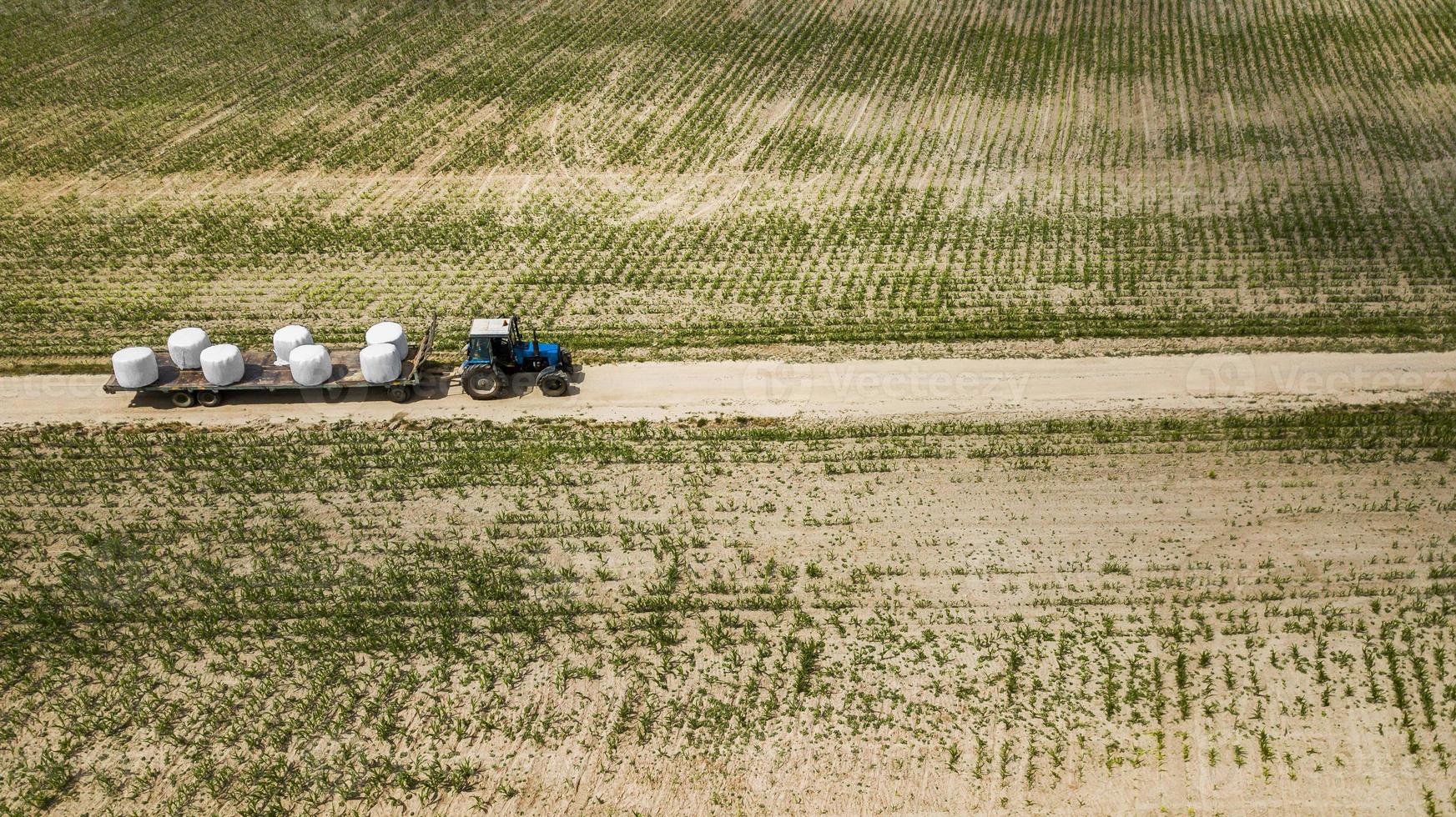 tractor rides on the field and carries bales of hay aerial view photo