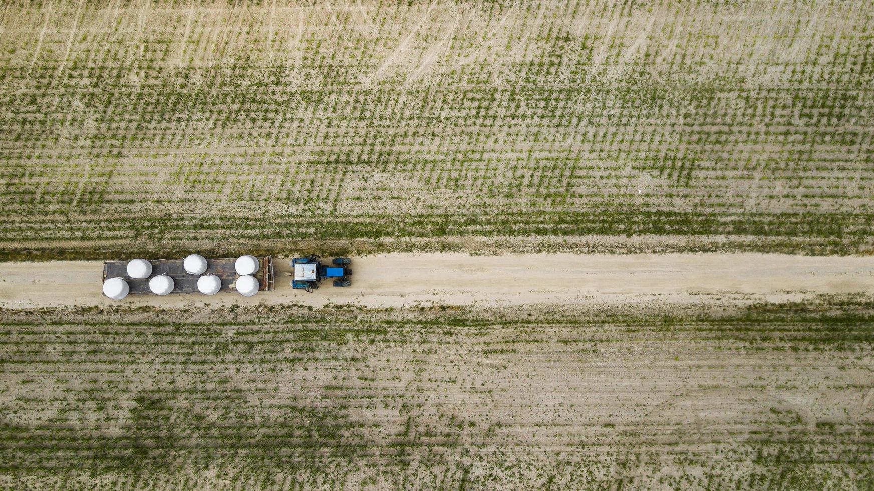 tractor rides on the field and carries bales of hay aerial view photo