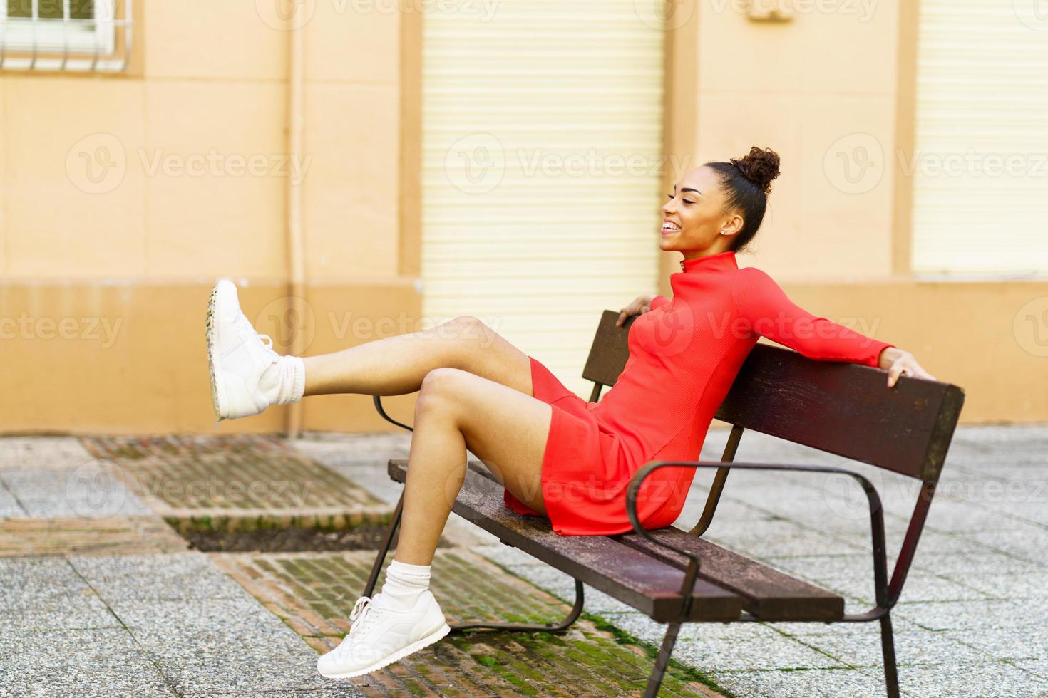 feliz mujer mixta, moviendo las piernas con alegría, sentada en un banco en  la calle. 5885578 Foto de stock en Vecteezy