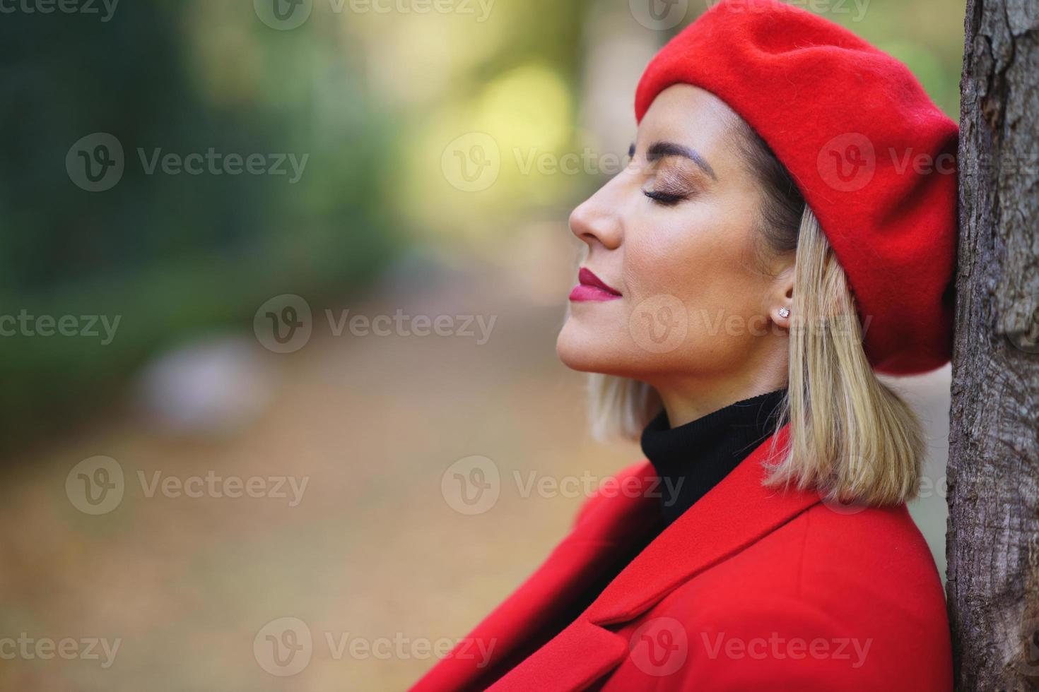 Close-up profile picture of a middle-aged woman leaning against a tree trunk with her eyes closed. photo