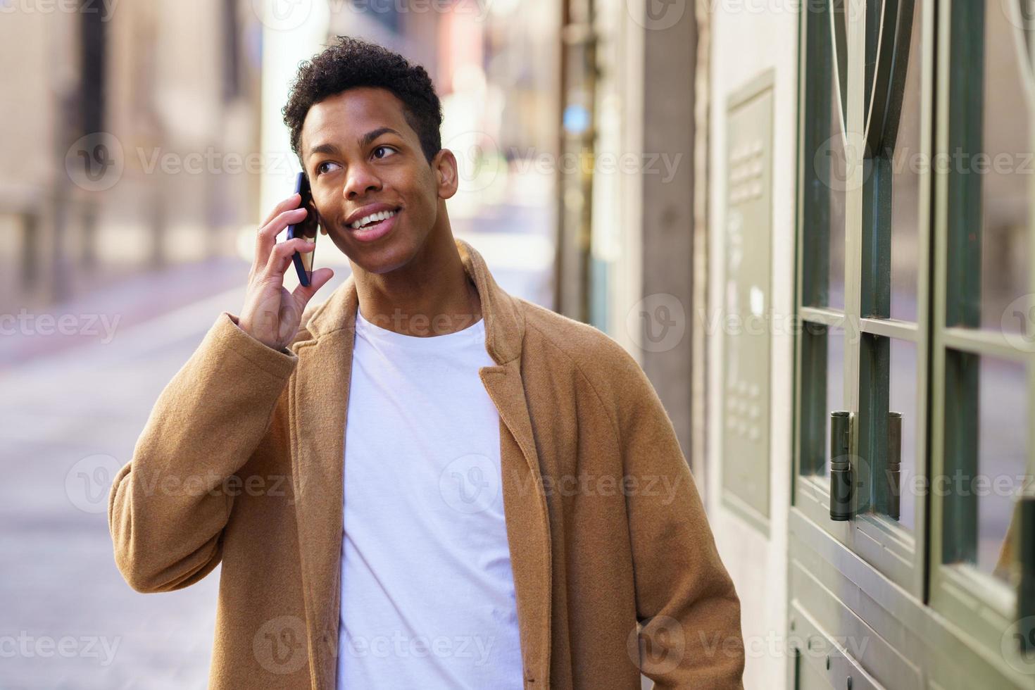 Young black man talking on the phone while walking down the street. photo