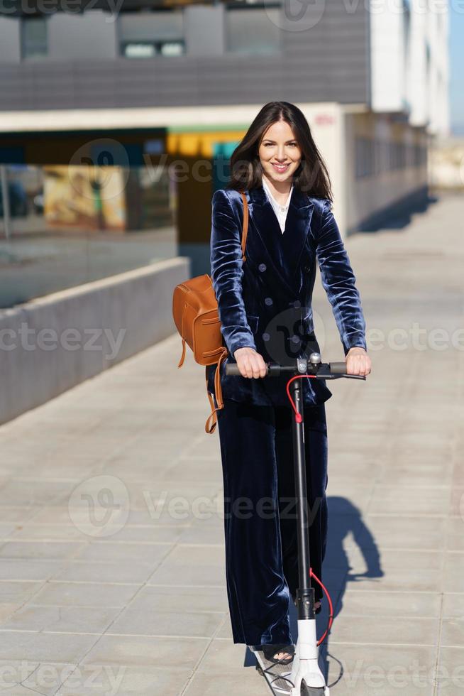 mujer de negocios joven con traje azul usando scooter eléctrico. foto