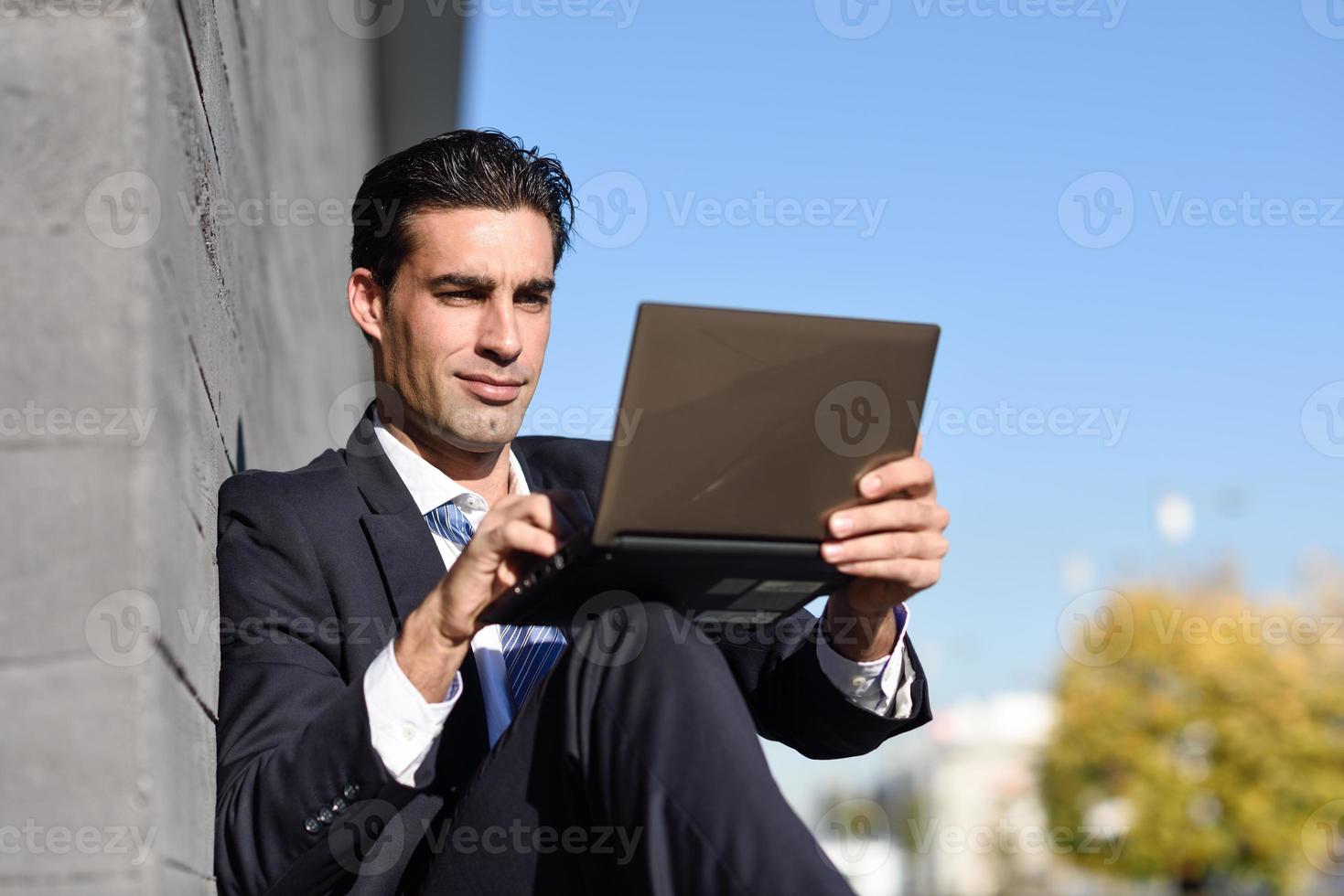 Businessman using a laptop computer sitting in the street photo