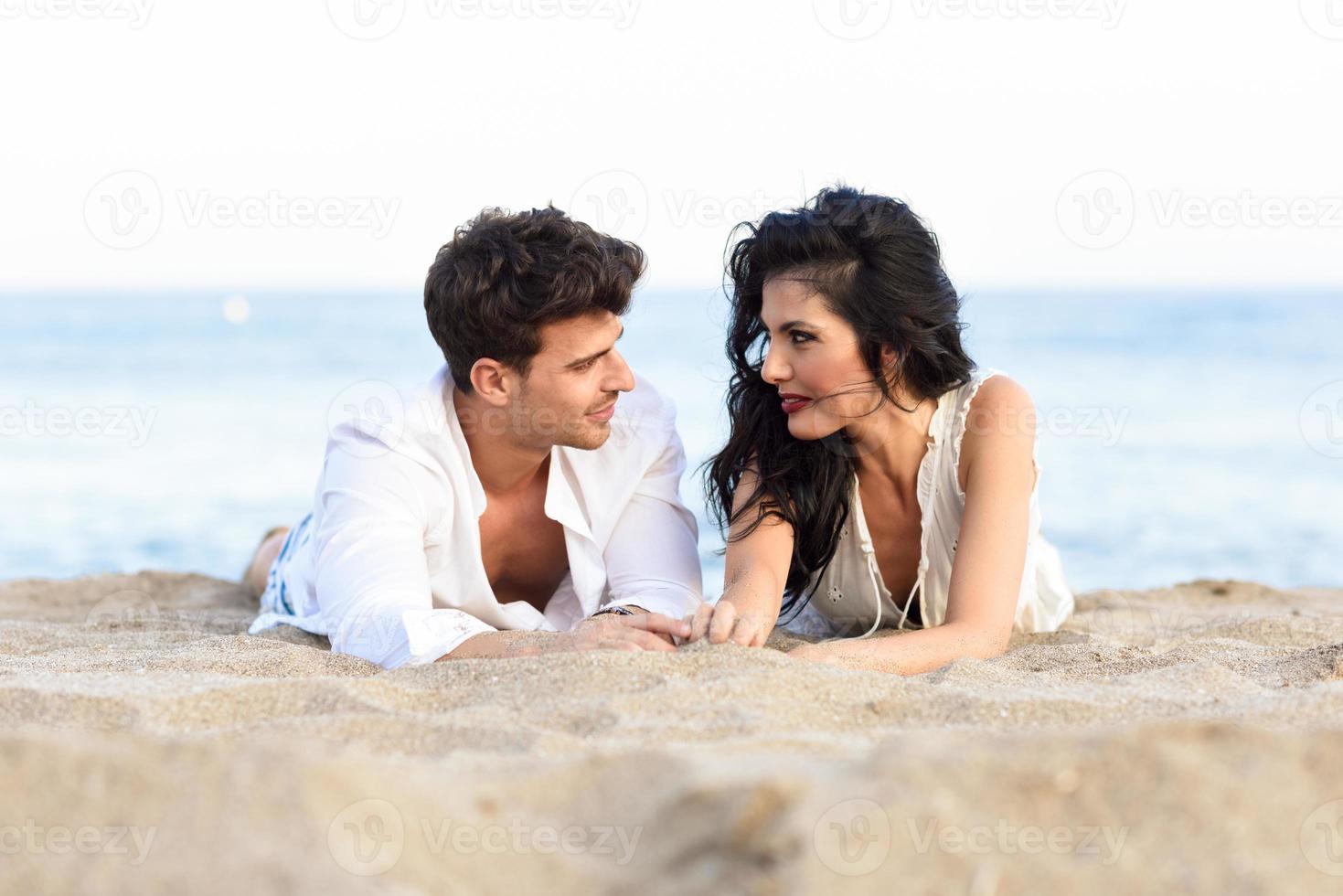 joven pareja feliz tirada en la arena en una hermosa playa foto