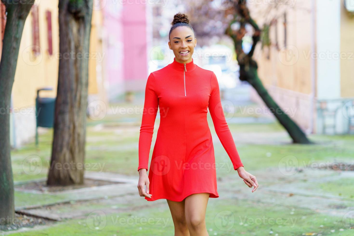 mujer mixta sonriente con vestido rojo caminando por la calle