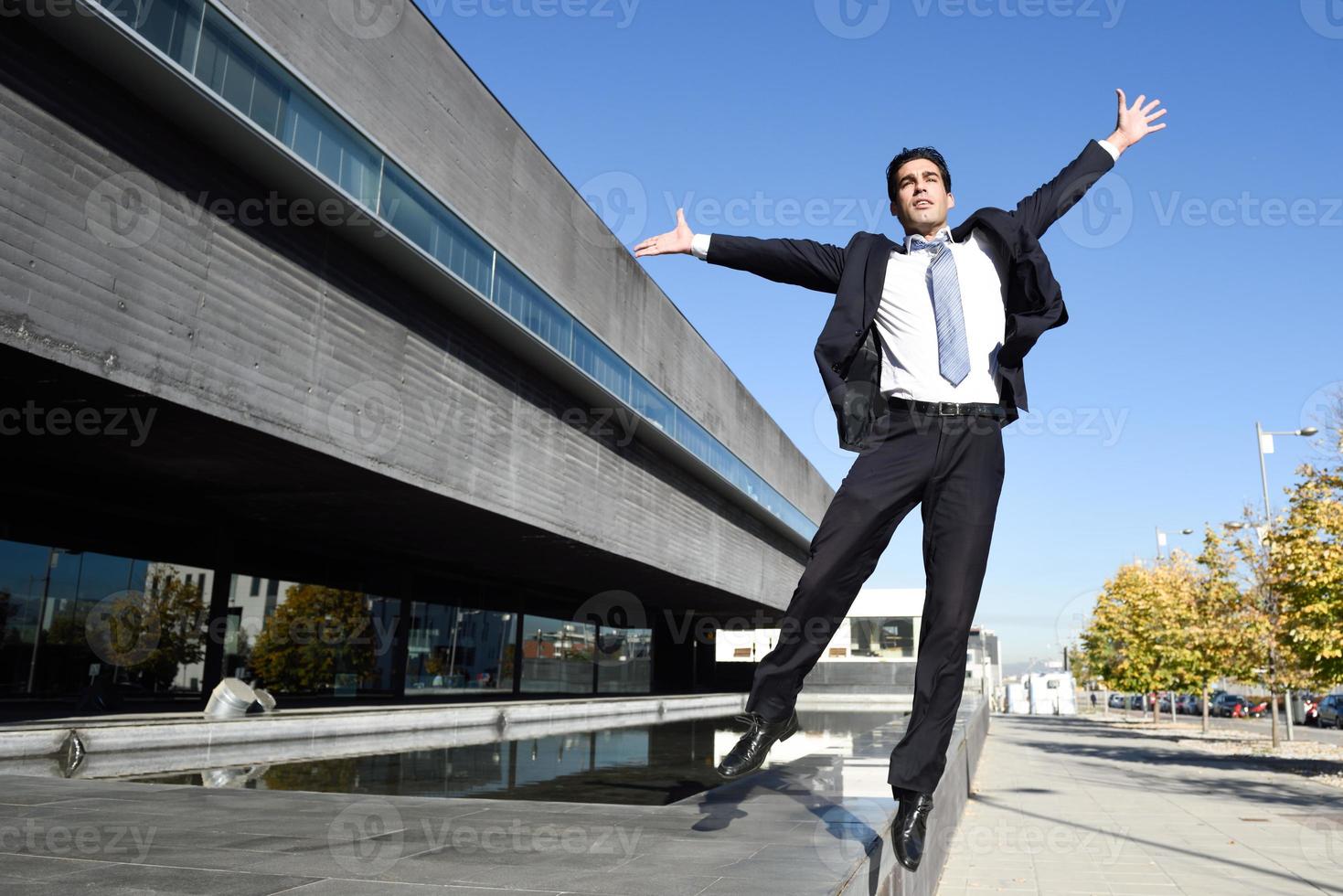 Businessman wearing blue suit and tie jumping in urban background photo