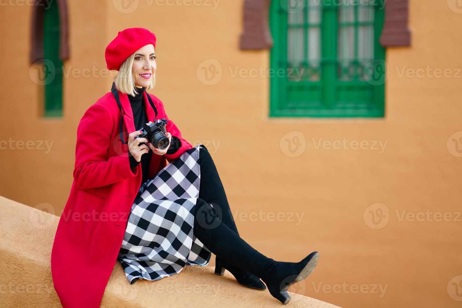 Woman wearing red winter clothes, taking pictures with an SLR camera sitting on a city wall. photo