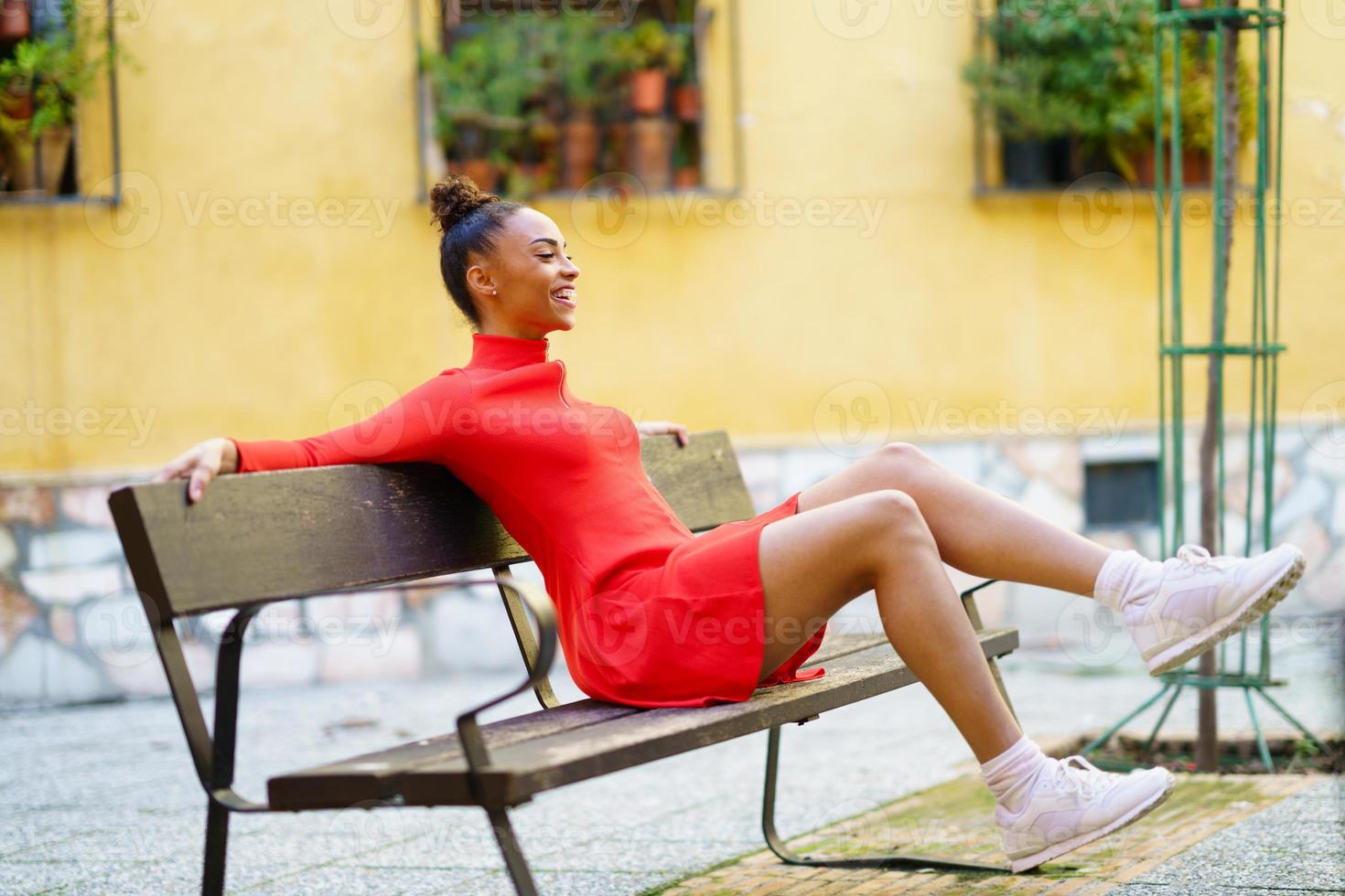 feliz mujer mixta, agitando las piernas con alegría, sentada en un banco en  la calle. 5889615 Foto de stock en Vecteezy