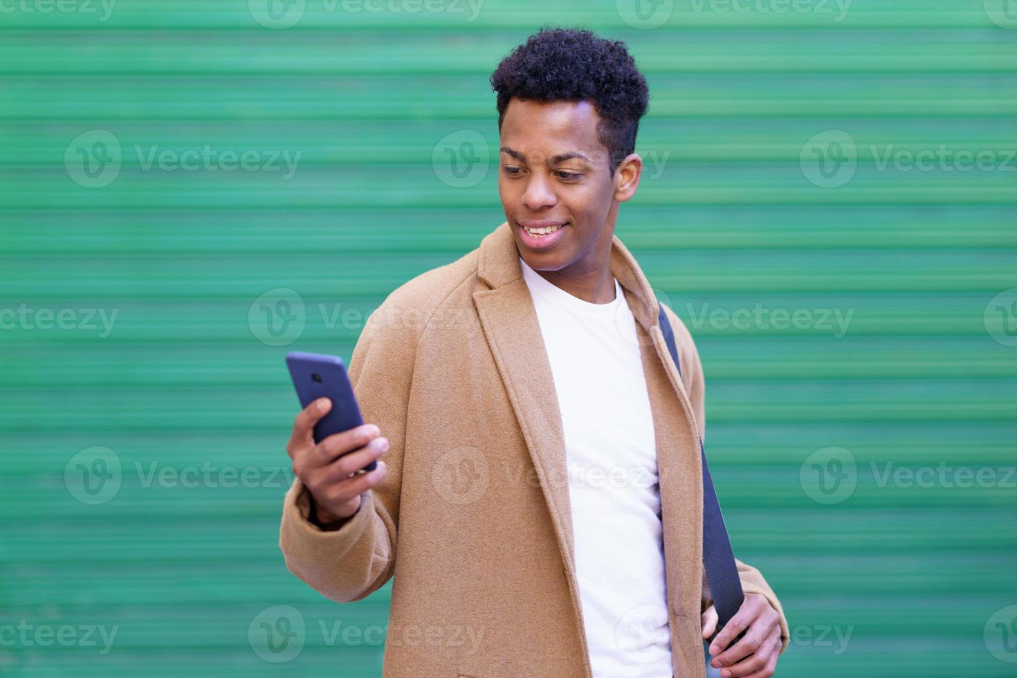 joven cubano usando un teléfono inteligente cerca de una pared urbana. foto