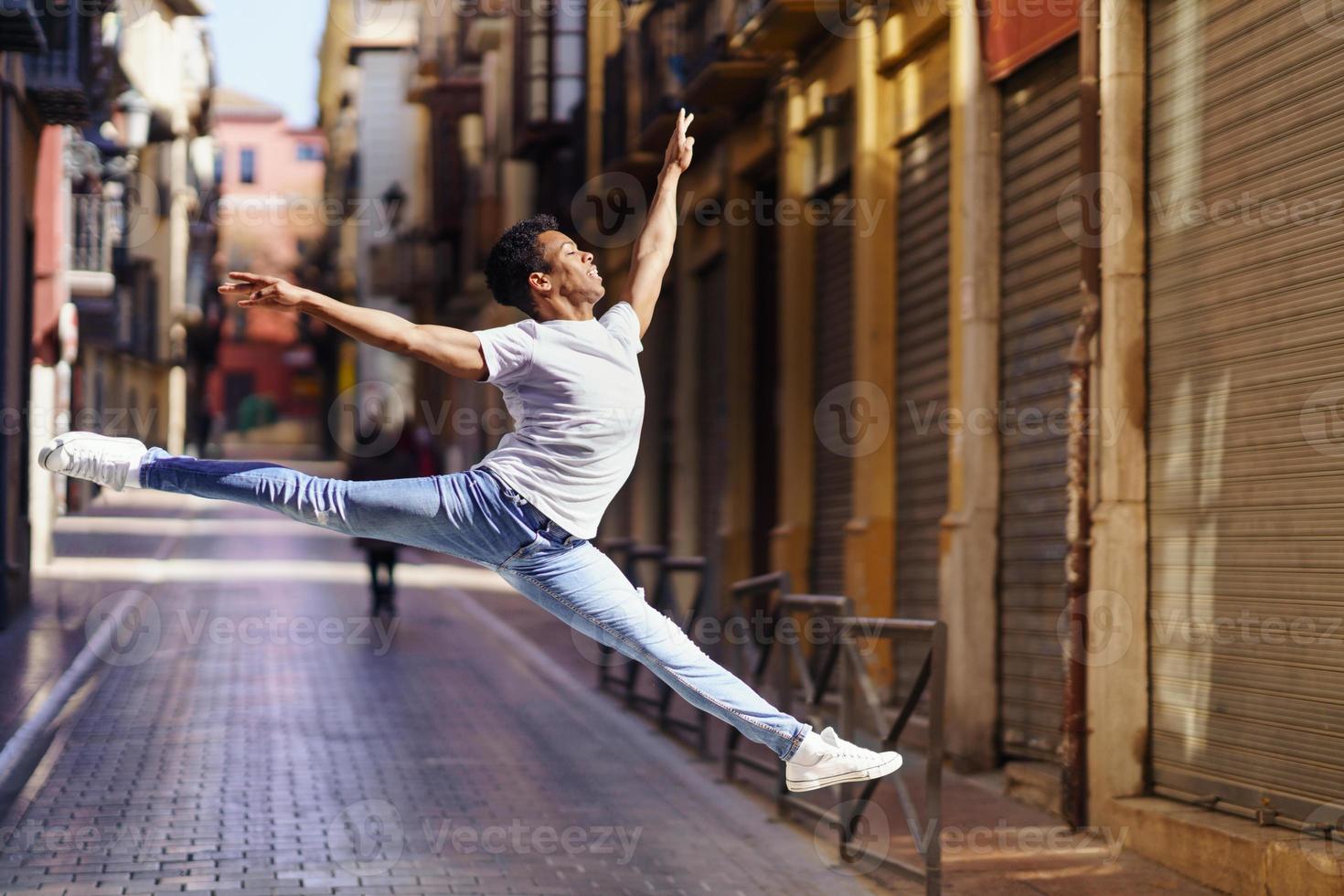 Young black man doing an acrobatic jump in the middle of the street. photo