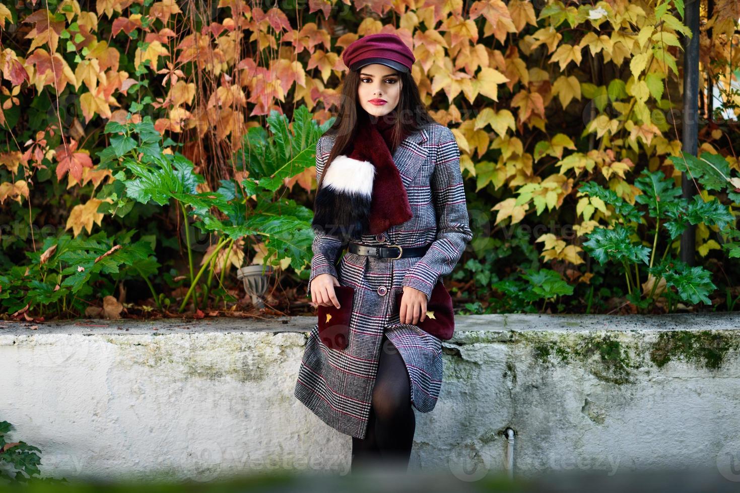 hermosa joven con el pelo muy largo con abrigo de invierno y gorra en el fondo de las hojas de otoño foto