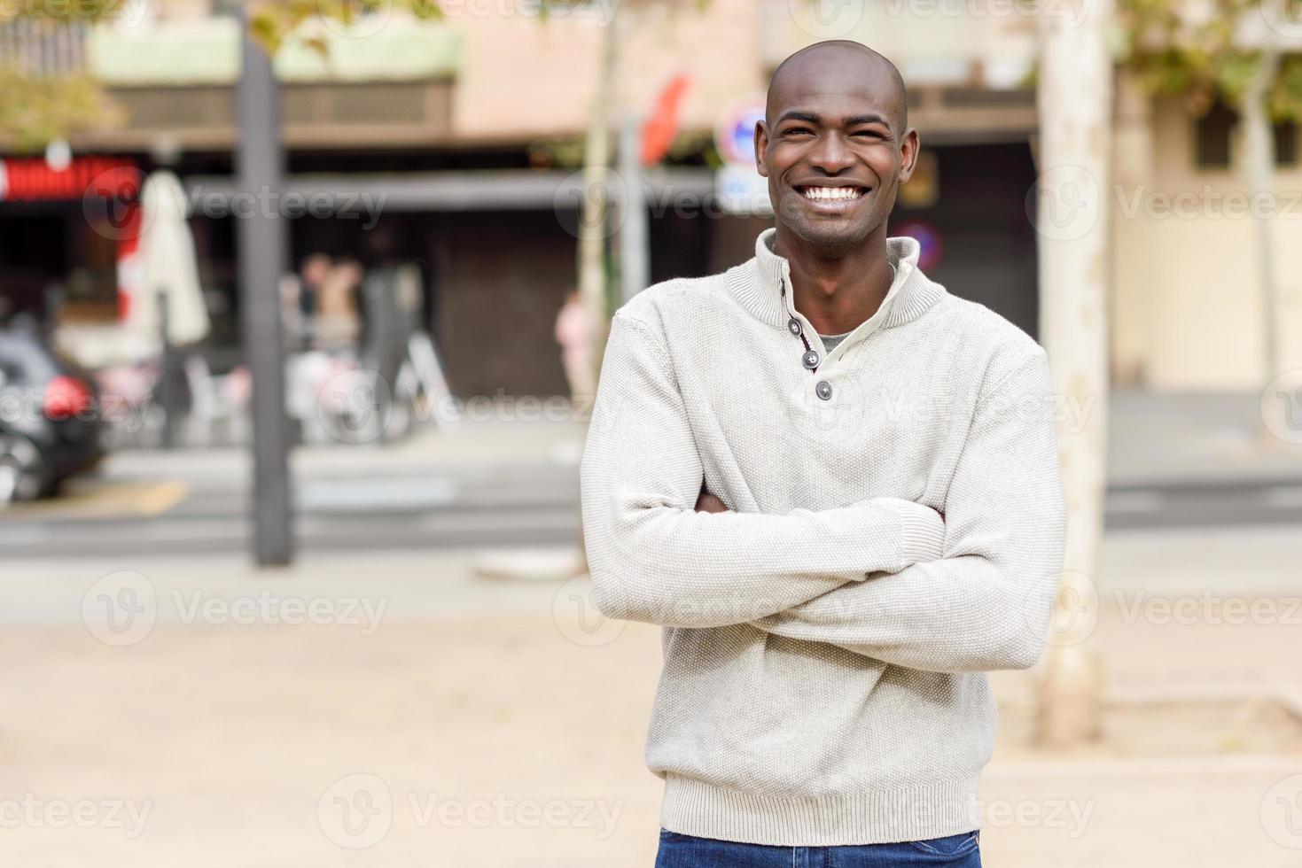 Black young man with arms crossed smiling in urban background photo