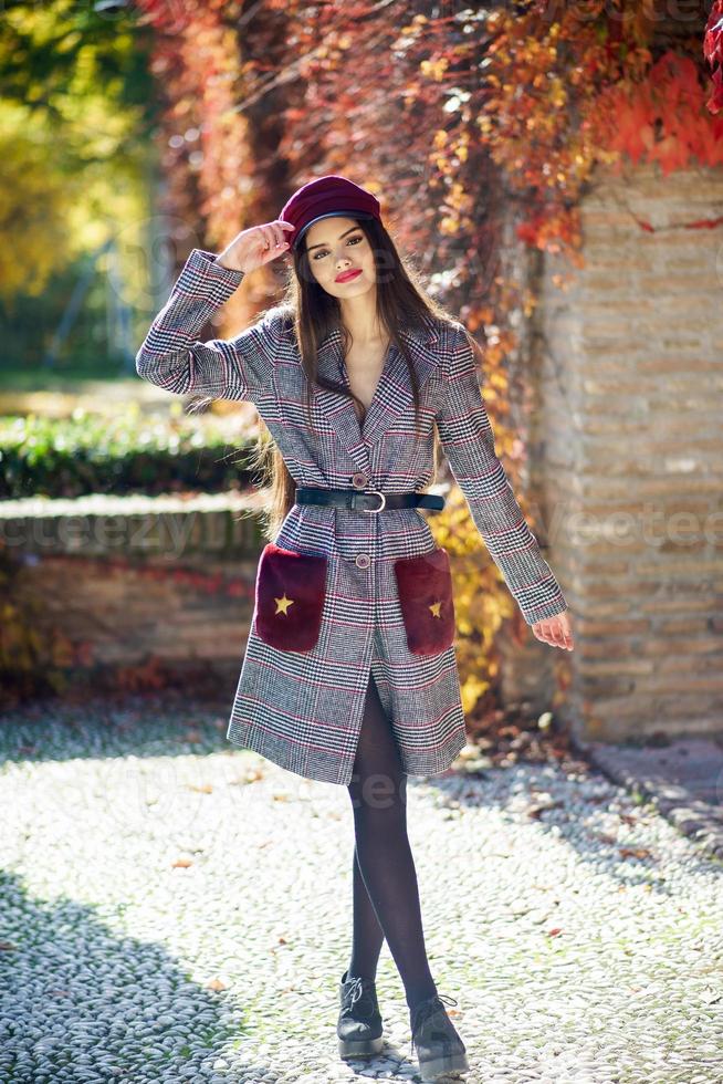 Young beautiful girl wearing winter coat and cap in autumn leaves background. photo