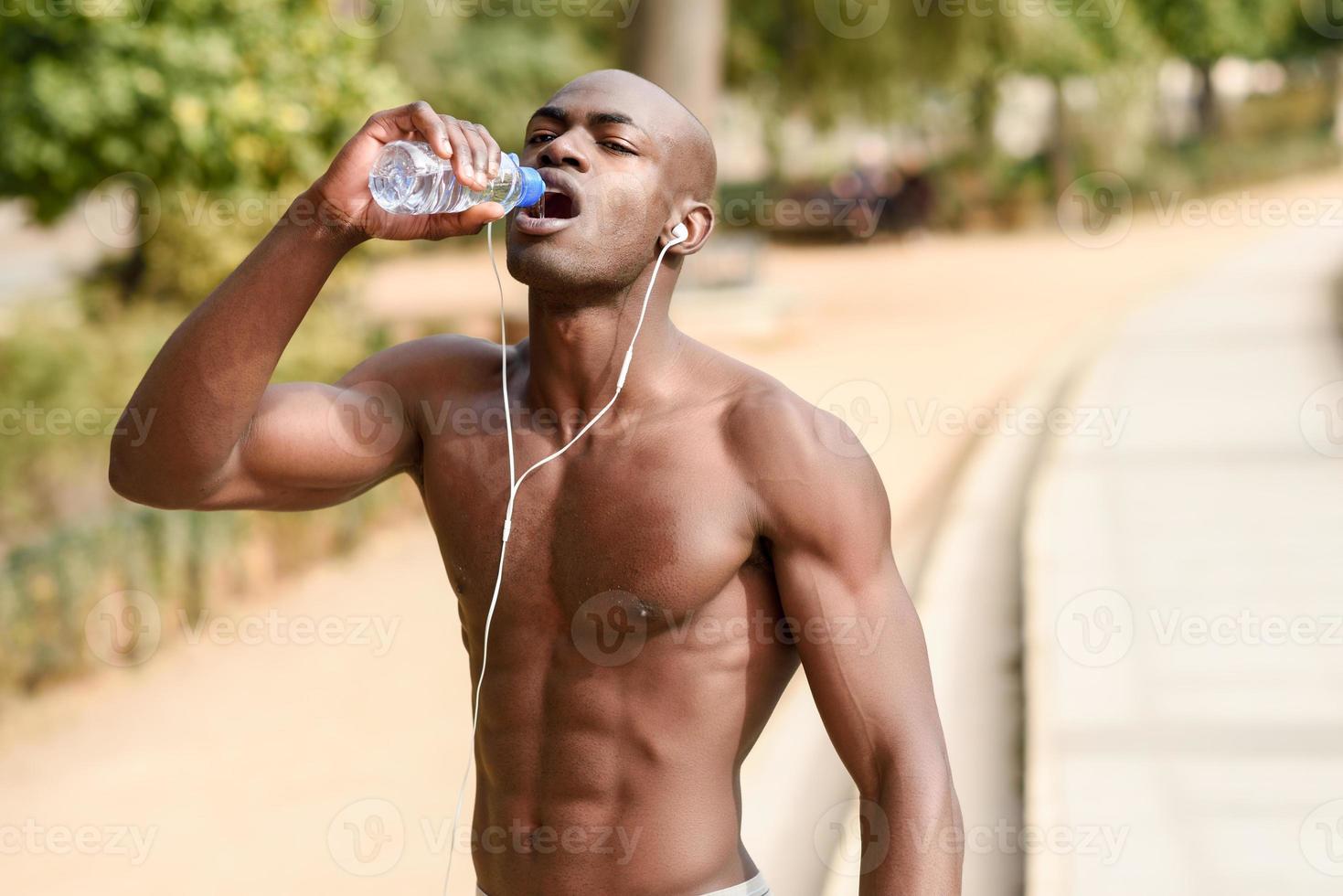 Black man drinking water after running in urban background. photo