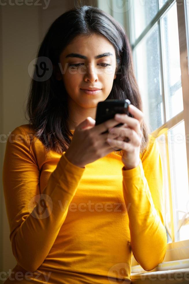 mujer persa usando su teléfono inteligente cerca de la ventana foto