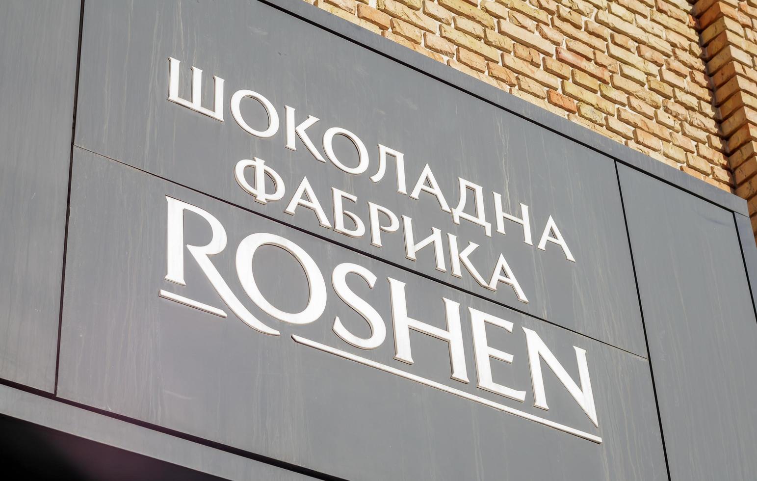 The main entrance to the building of the Roshen confectionery chocolate factory in Kiev. White letters in Ukrainian on a black sign. Emblem of the Roshen company. Ukraine, Kiev - February 09, 2022. photo