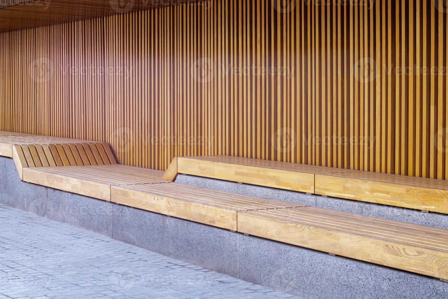 Empty modern wooden benches without people on a sunny day, public places in the city park. City improvement, urban planning, public spaces, recreation area. City public anti-vandal furniture for rest. photo
