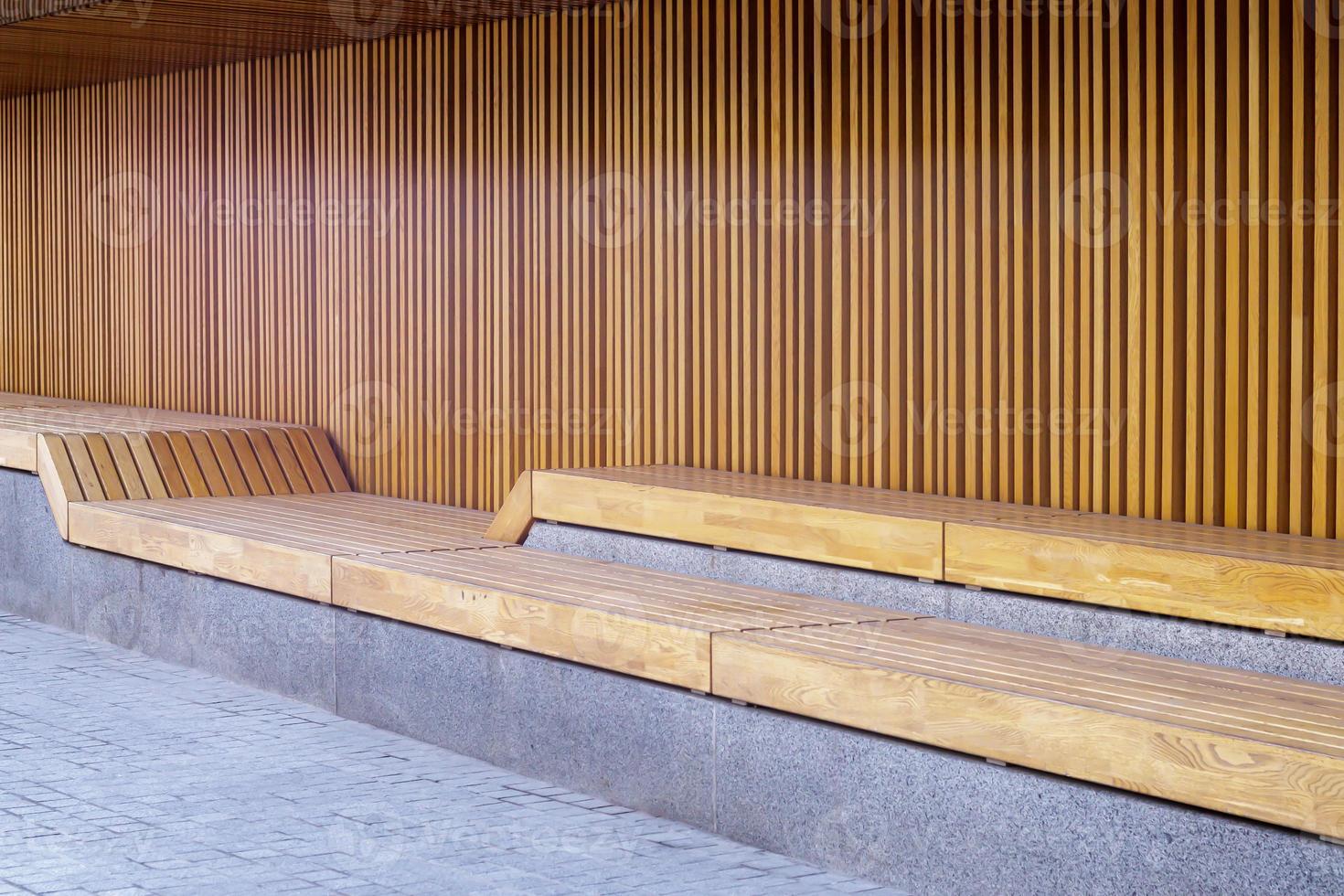 bancos de madera modernos vacíos sin gente en un día soleado, lugares públicos en el parque de la ciudad. mejora de la ciudad, urbanismo, espacios públicos, zona de recreo. Mobiliario público urbano antivandálico para el descanso. foto