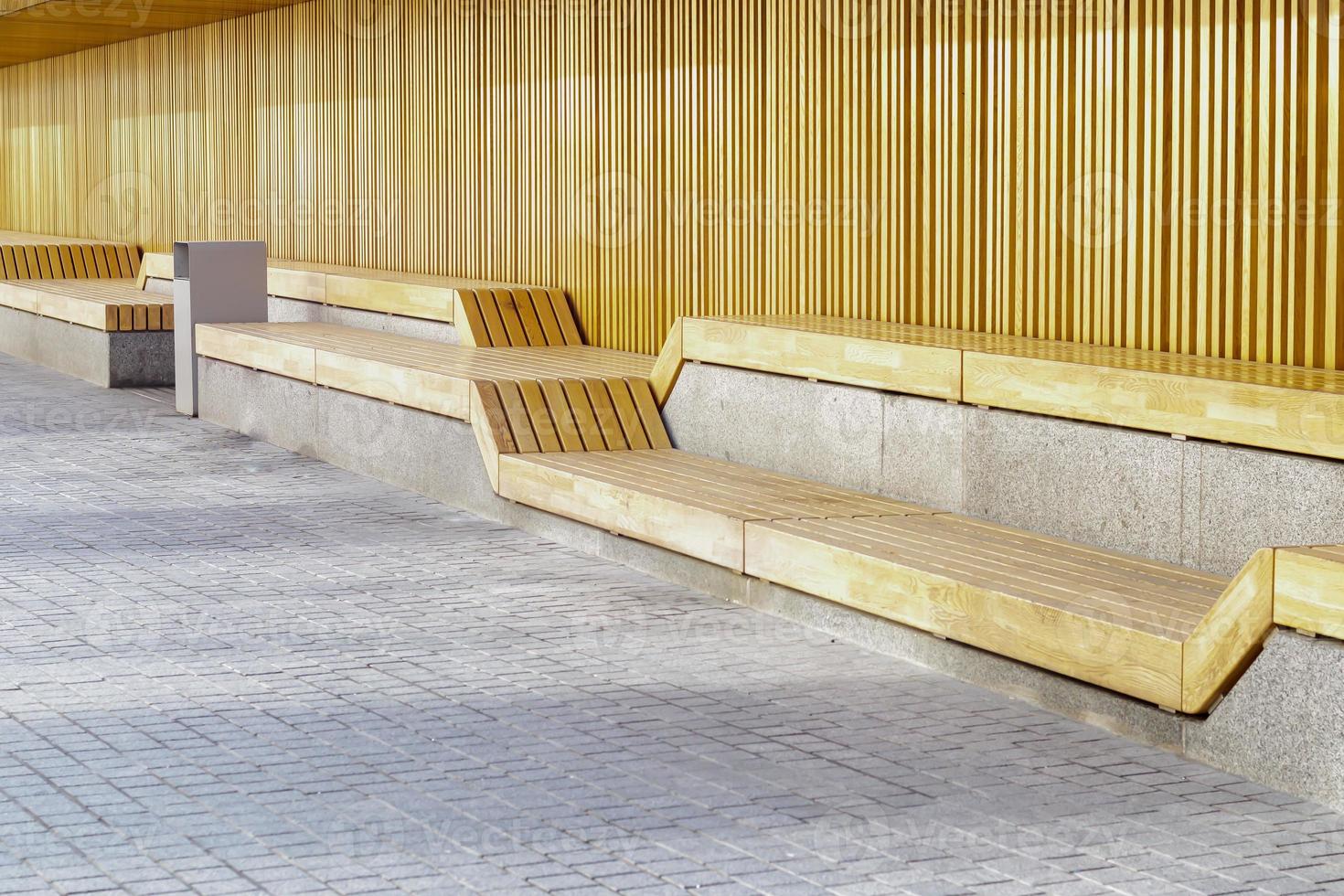 Empty modern wooden benches without people on a sunny day, public places in the city park. City improvement, urban planning, public spaces, recreation area. City public anti-vandal furniture for rest. photo