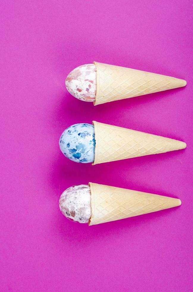 Vanilla ice cream waffle horns with decoration eggs on pink background. Minimalism. Creative Easter concept. Studio Photo