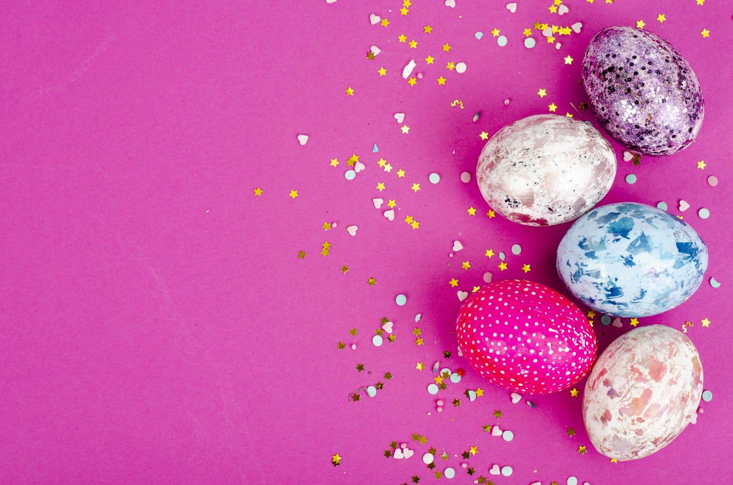 Multicolored handmade easter eggs and confetti on pink background. Minimal concept. View from above. Space for text. Studio Photo