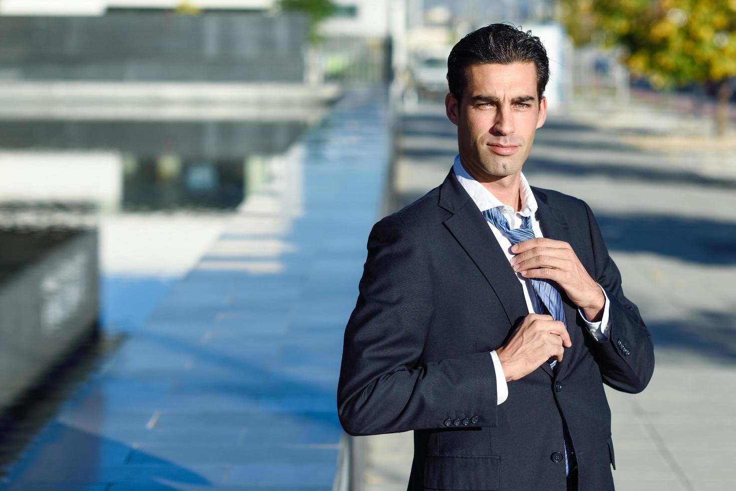 Young handsome businessman adjusting a tie in urban background photo