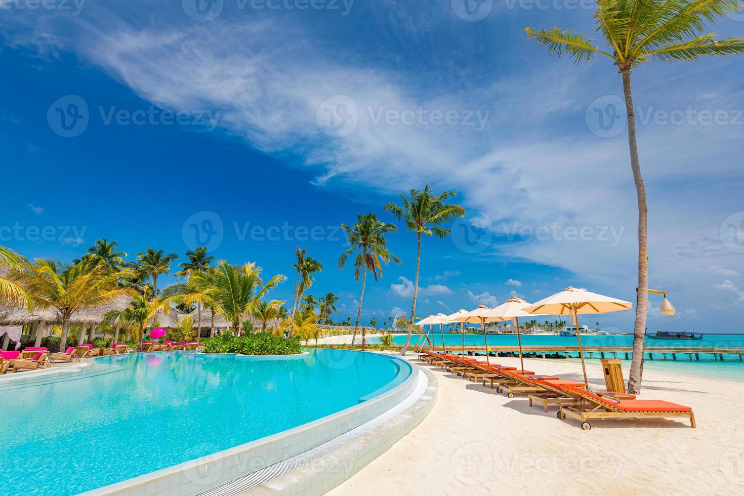 Outdoor tourism landscape. Luxurious beach resort with swimming pool and beach chairs or loungers under umbrellas with palm trees and blue sky. Summer travel and vacation background concept photo